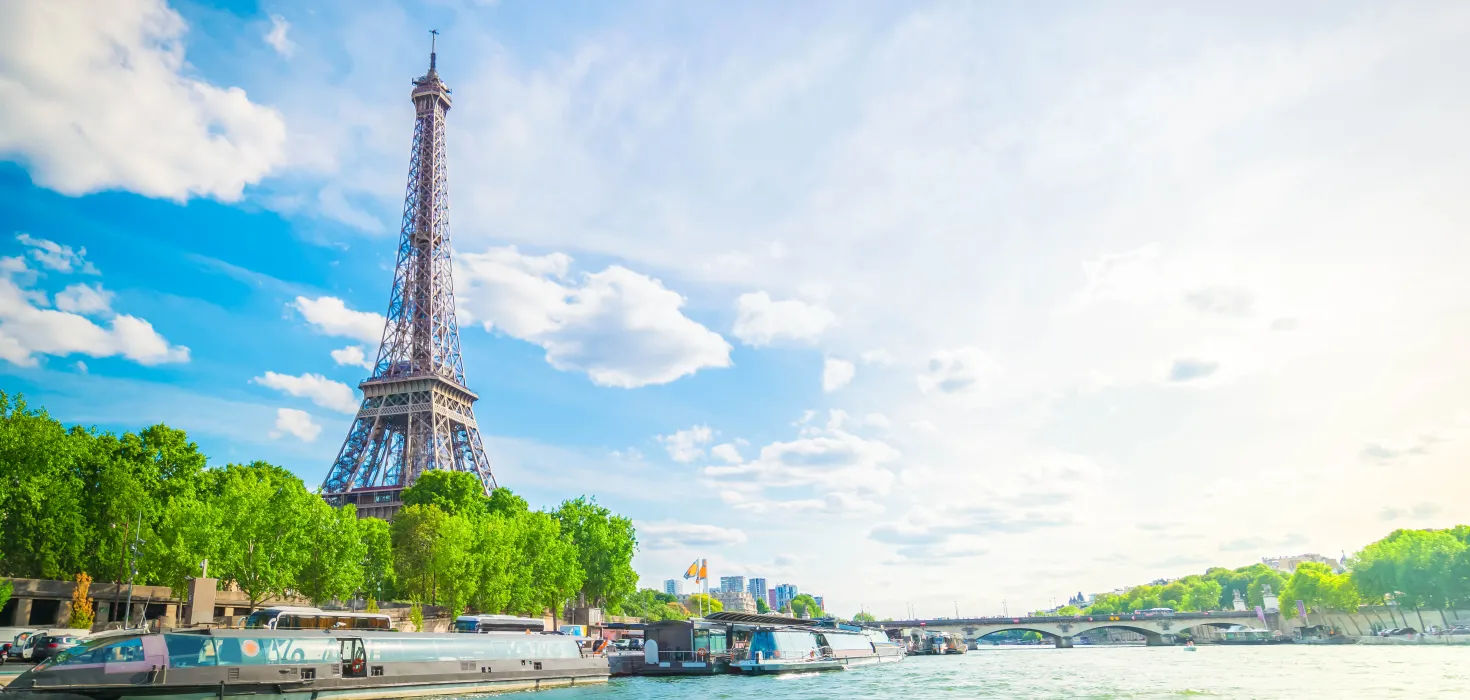 The Eiffel Tower by the Seine, surrounded by green trees and boats