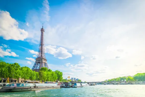 The Eiffel Tower by the Seine, surrounded by green trees and boats