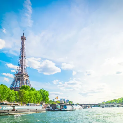 La Torre Eiffel junto al Sena, rodeada de árboles verdes y barcos